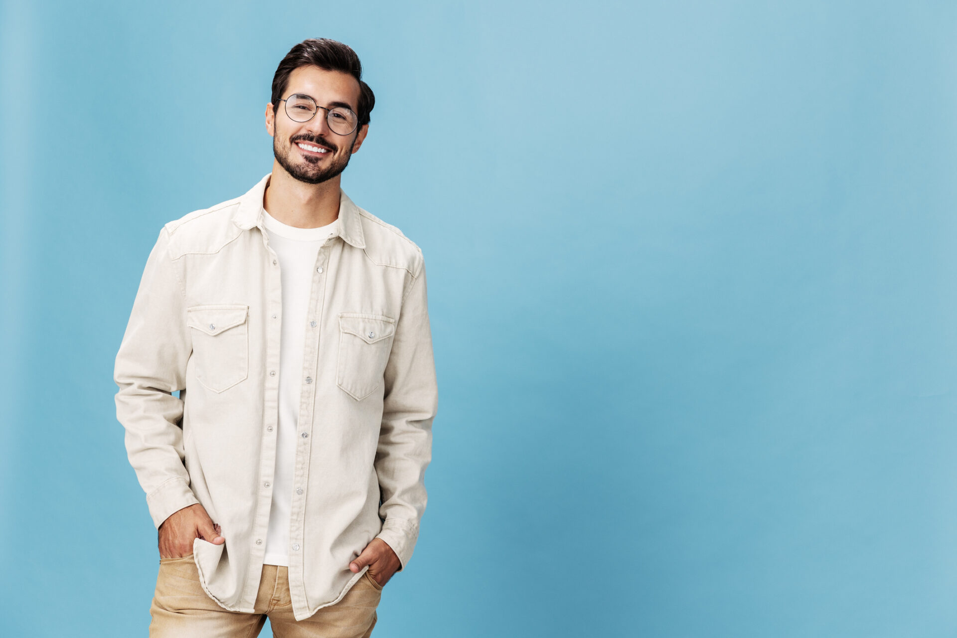 Portrait of a stylish man smile with teeth in glasses for farsightedness and myopia, on a blue background in a white T-shirt, fashionable clothing style, space space Portrait of a stylish man smile with teeth in glasses for farsightedness and myopia, on a blue background in a white T-shirt, fashionable clothing style, space space. High quality photo